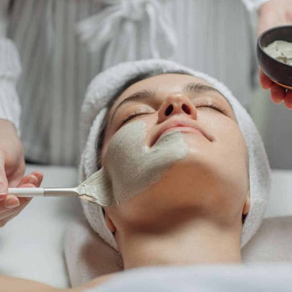 Cosmeotologist Applying a Facial Mask Caucasian cosmetologist woman applying a facial mask on a beautiful young Caucasian woman's face lying on the massaging bed.