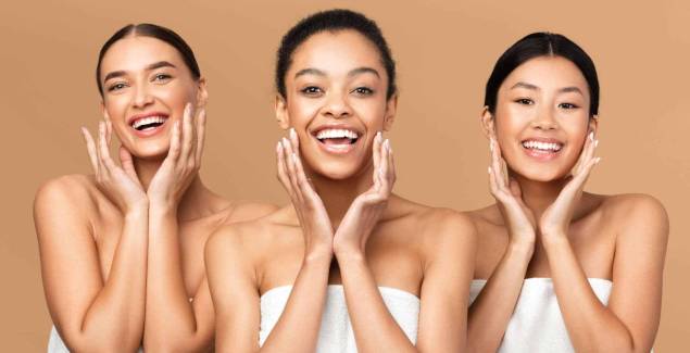 Skincare And Beauty. Three Multiracial Girls Touching Face With Perfect Smooth Skin On Cheeks Smiling At Camera Over Beige Background
